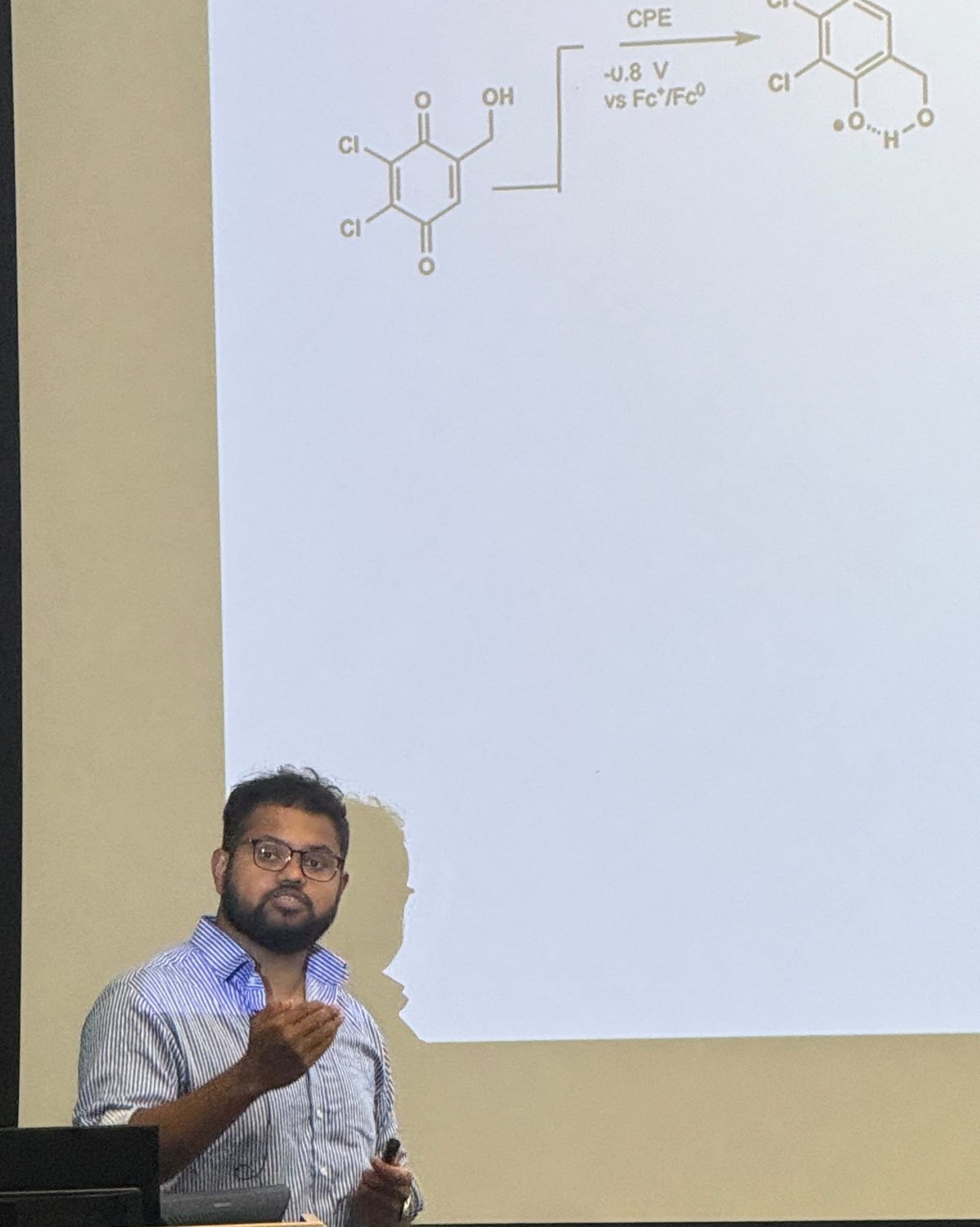 Partho K. Paul presenting his research, with a quinone reduction scheme on the screen behind him